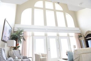 Un salon spacieux avec un plafond haut, de grandes fenêtres en arc de cercle et une cheminée.
