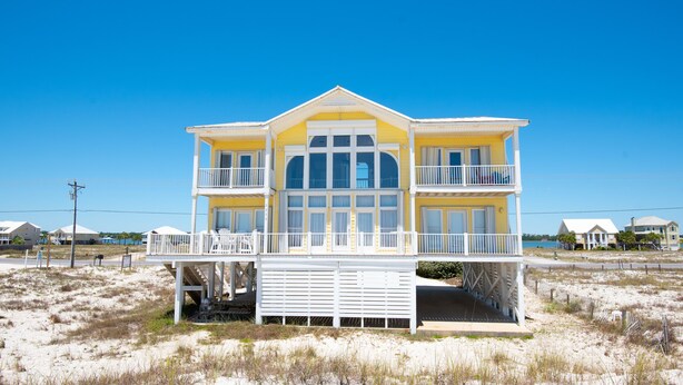 A two-story beach house with a balcony, a covered front porch, and a large window.