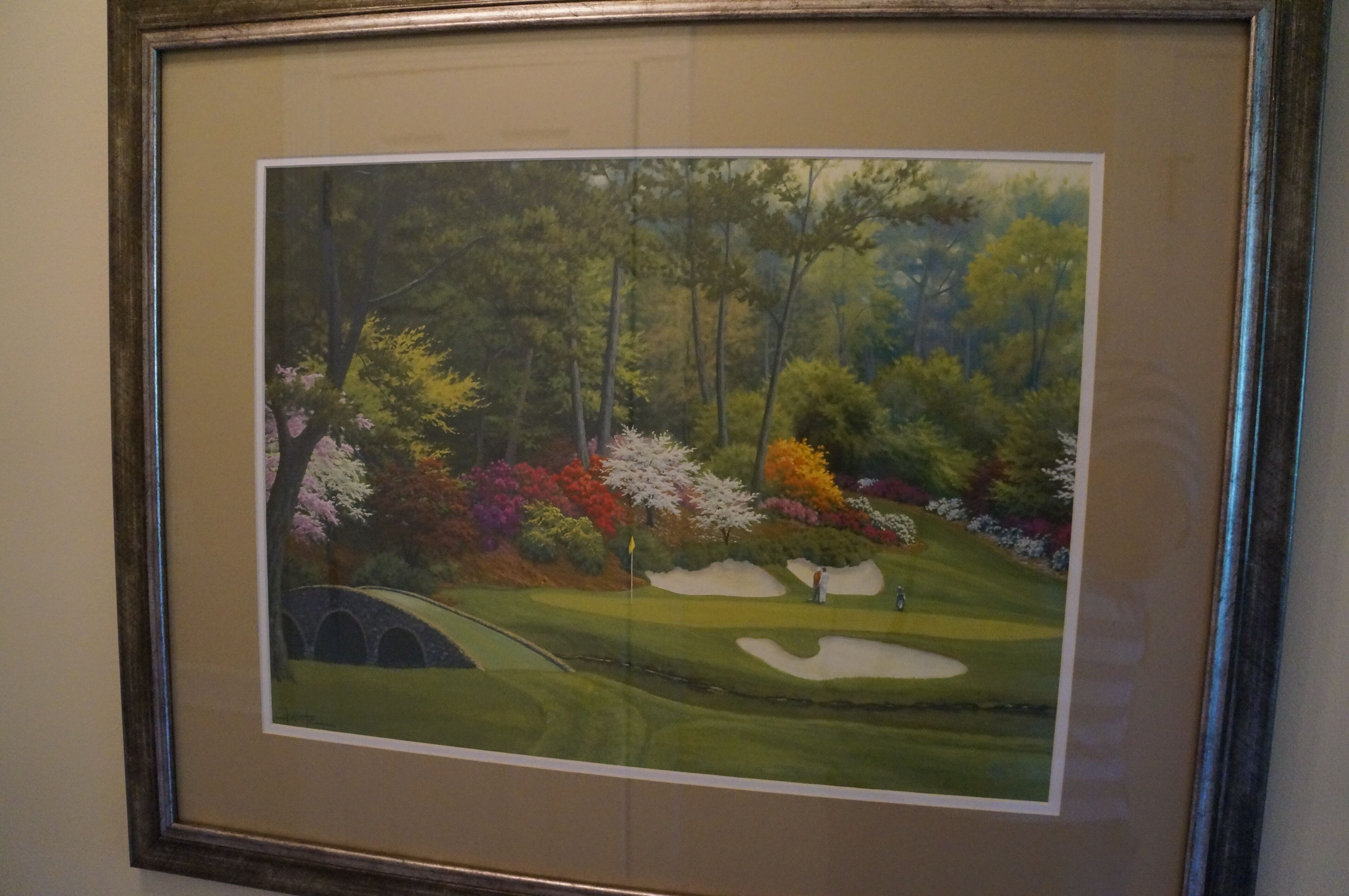 Pintura emoldurada de uma paisagem com um campo de golfe, árvores e uma ponte.
