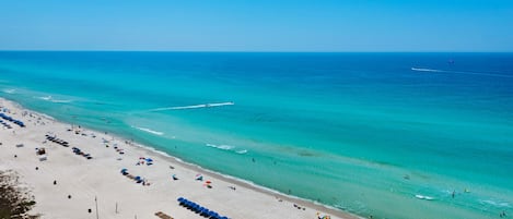 A beach with rows of umbrellas and sun loungers, a clear blue sky, and calm sea.