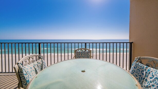 A balcony with a table and chairs, overlooking a beach and the ocean. - Ocean Breeze Escape Phoenix X 1010 (Orange Beach)