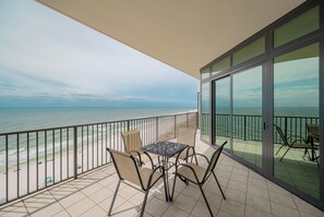A balcony with a table and chairs, overlooking a beach and the sea.