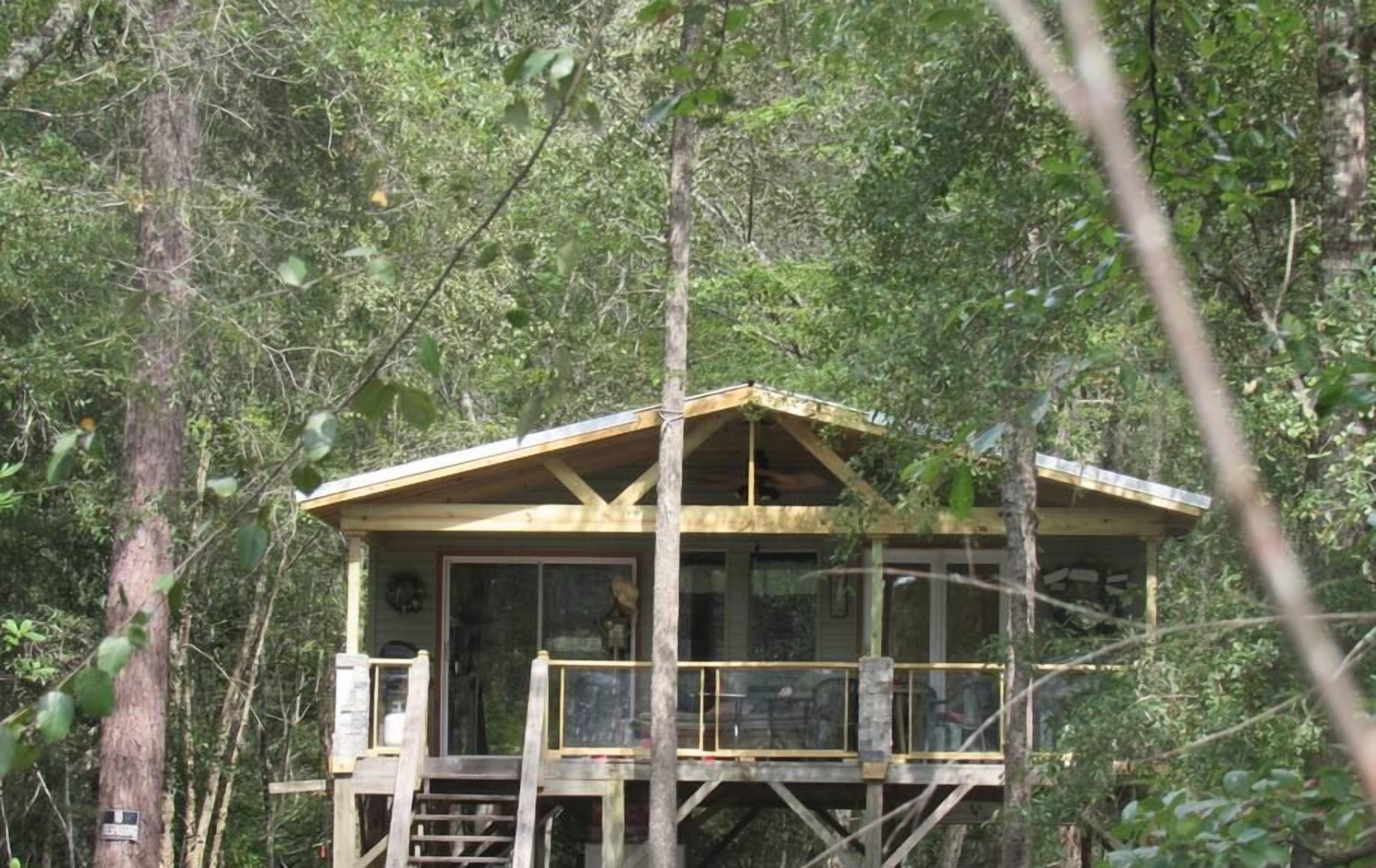Una cabaña de madera de dos pisos con un balcón, rodeada de un bosque denso.
