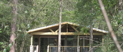 Une cabane en bois à deux étages, dotée d’un balcon et entourée d’une forêt dense.