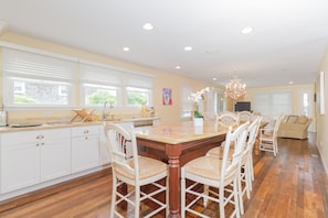 A spacious kitchen with white cabinetry, a wooden dining table surrounded by chairs, and a chandelier.