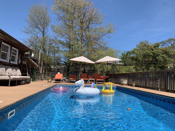 Una piscina con juguetes inflables de cisne y delfín, rodeada de sillones de descanso y sombrillas.