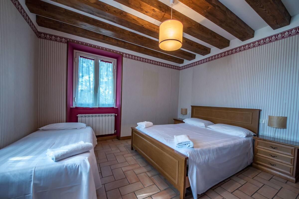 A hotel room with two beds, a wooden ceiling, a window, and a radiator.