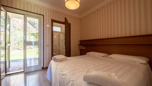 Hotelkamer met een groot bed, een houten hoofdeinde, een schuifdeur van glas naar een buitenruimte en een plafondlamp.
