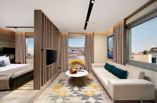 A modern hotel room with a bed, sofa, TV, and a dining table with a fruit bowl. - Nish Palace Exclusive Suites (Istanbul)