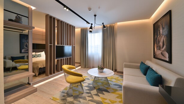 Una sala de estar moderna con un sofá, un sillón y una mesa de centro, un televisor de pantalla plana y una gran estatua de Buda en la pared.