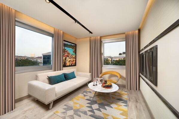 Un salon moderne avec un canapé, un fauteuil et une table basse, de grandes fenêtres et un tableau accroché au mur.