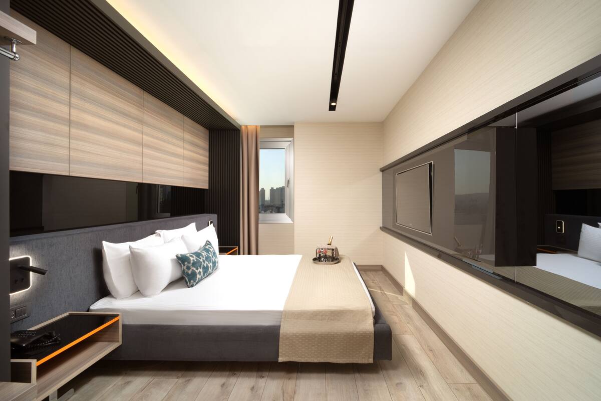 Una habitación de hotel moderna con una cama grande, mesitas de noche, televisión y vistas a la ciudad.