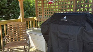 Une terrasse extérieure couverte, équipée d’un barbecue, d’une chaise en bois et d’une clôture à treillis.