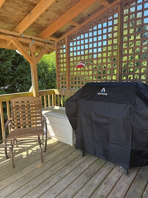Une terrasse extérieure couverte, équipée d’un barbecue, d’une chaise en bois et d’une clôture à treillis.