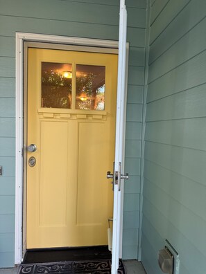 A yellow door with a window, a doormat, and a doorbell.