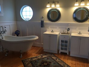 Un baño con una bañera independiente, dos lavamanos y un espejo redondo con un borde decorativo.
