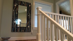 Un escalier avec des rampes blanches mène à un palier. Un miroir décoratif orné d’un motif en mosaïque est accroché au mur, au-dessus du palier.