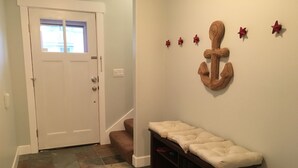 Un couloir avec une porte blanche, un banc doté d’un espace de rangement, un tapis à motifs et des éléments de décoration murale, notamment des étoiles et une ancre.