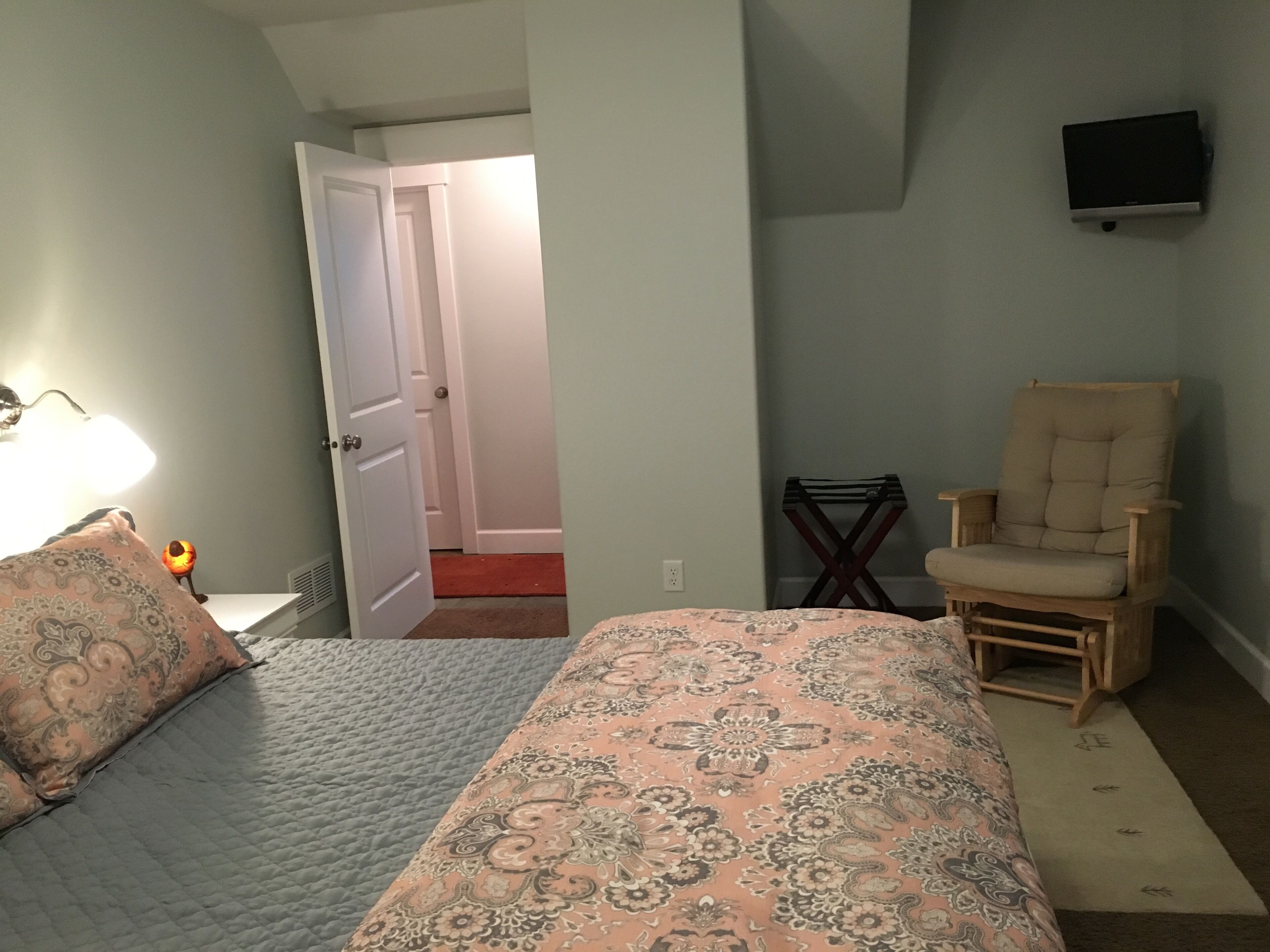 A bedroom with a bed, a chair, and a TV on the wall.
