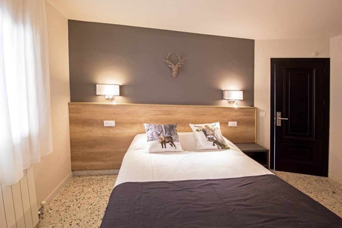 A hotel room with a large bed, two wall-mounted lamps, a wooden headboard, and a deer head decoration.