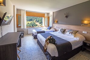 Habitación de hotel con dos camas, un escritorio y una ventana con vista al bosque.
