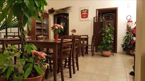 A dining area with wooden tables and chairs, surrounded by potted plants.