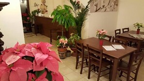 A dining area with wooden tables and chairs, potted plants, and a reception desk with decorative items. - Oasi di Francesca (Belpasso)