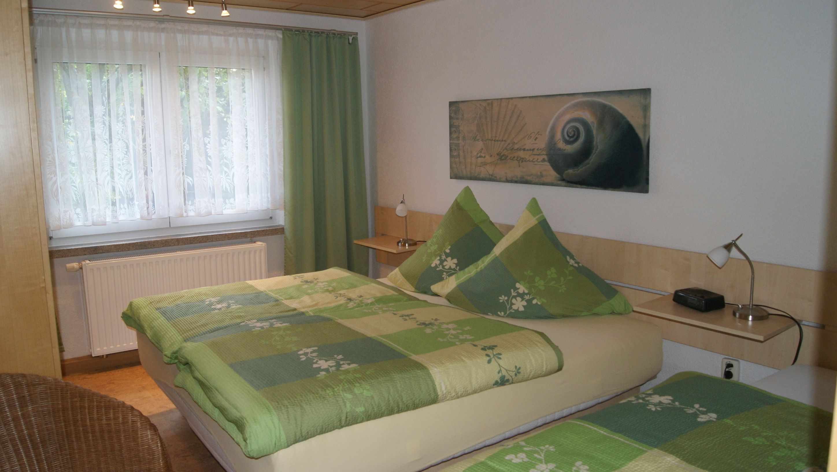 A bedroom with a bed, a nightstand, a lamp, a radiator, and a window with curtains.