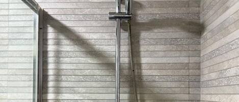 Ducha con manguera de mano en un cuarto con paredes de azulejos.