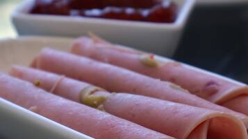 A table with various food items including ham rolls, a bowl of ketchup, and a plate with different dishes.