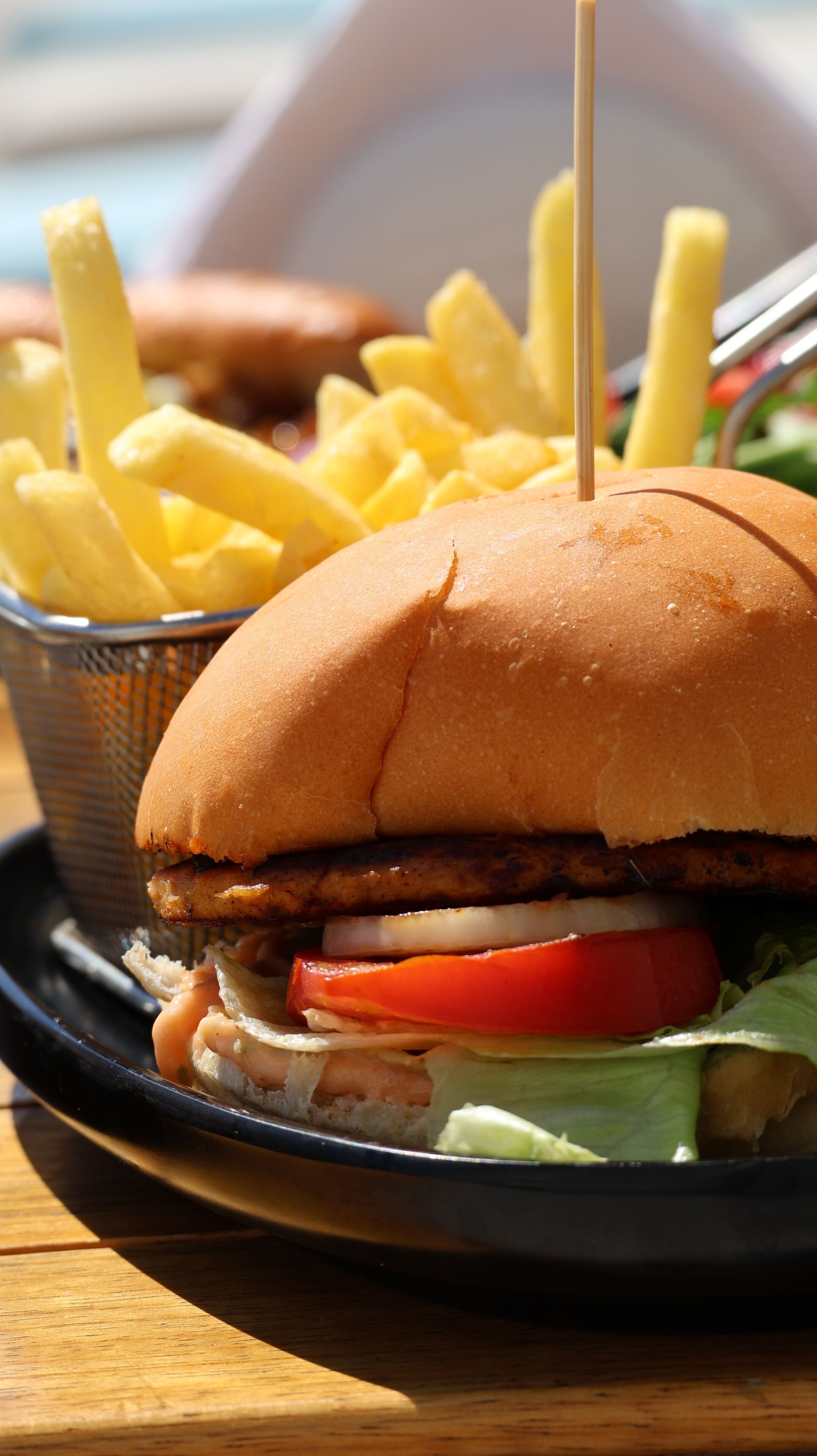 A sandwich with a bun, lettuce, tomato, and a meat patty, accompanied by a side of French fries.