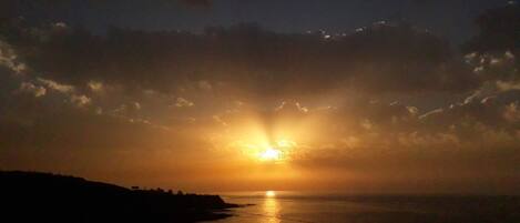 A sunset over a coastal landscape with a silhouette of a building in the foreground.