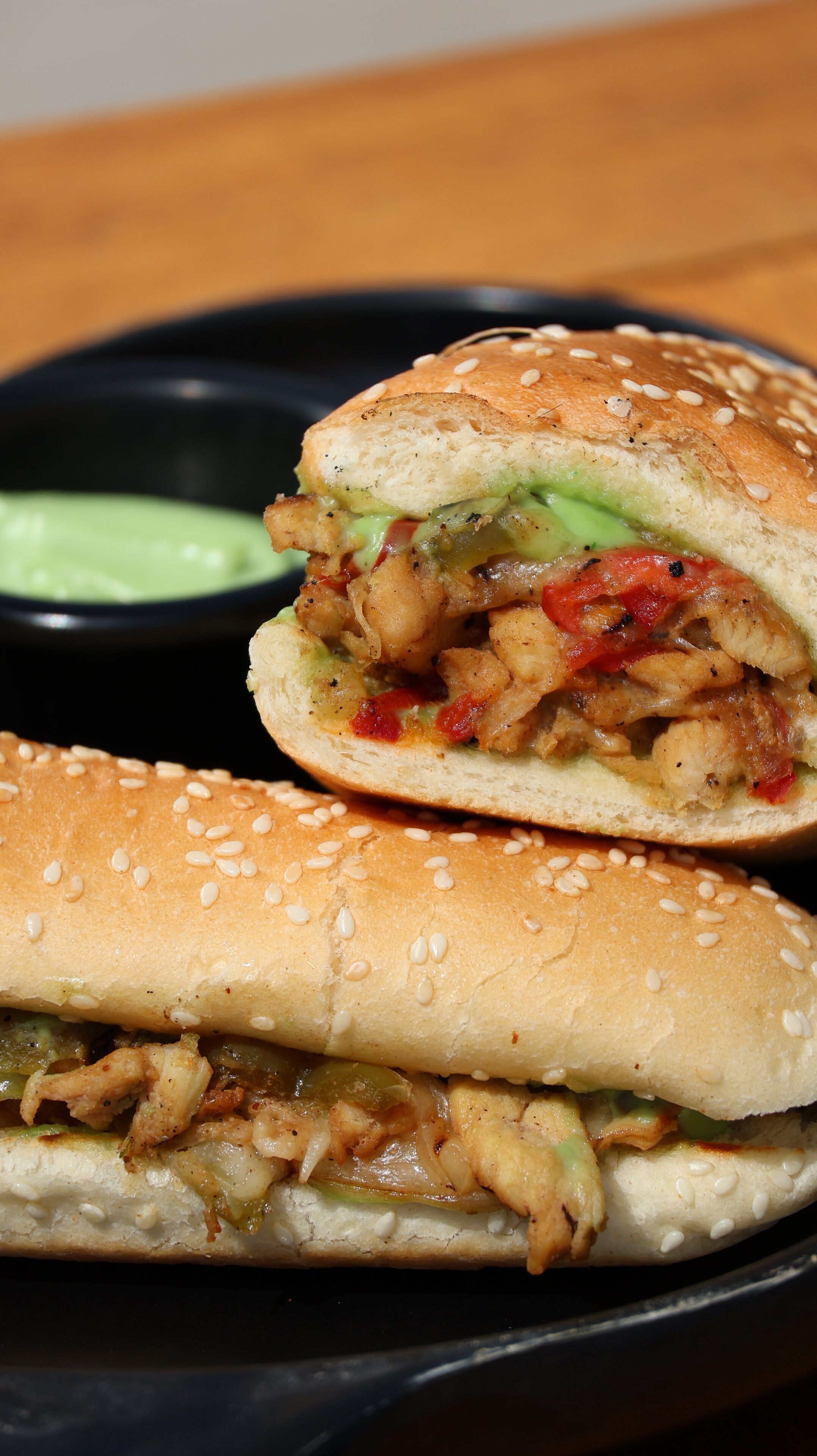 A sandwich with visible ingredients like chicken, vegetables, and sauce, served with a side of dipping sauce.