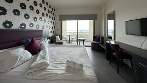 A hotel room with a large bed, a desk, a chair, a TV, and a balcony with a view. - Le Six Resort Hotel (Batroun)