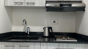 A modern kitchen with grey wood cabinets, a black countertop, stainless steel appliances, and a kettle. - Le Six Resort Hotel (Batroun)