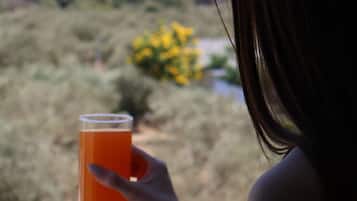 A person holding a glass of orange liquid, overlooking a landscape with hills and sparse vegetation.
