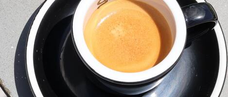 Una taza de café sobre un platito blanco y negro con un logotipo, colocada sobre una superficie gris.