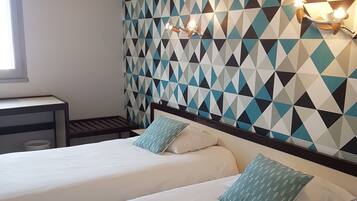 A hotel room with two beds, a geometric patterned wall, and a nightstand with a lamp.