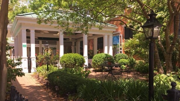 A covered outdoor area with a pathway leading to a building with columns. There are potted plants and a table with chairs. - Smithfield Inn (Smithfield)