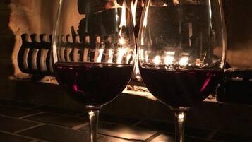 Two wine glasses filled with red wine, placed on a stone floor with a fire in the background.