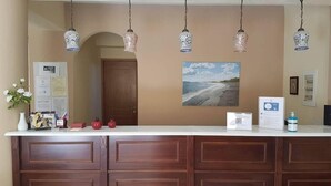 Un comptoir d’accueil avec un panneau en bois, un tableau représentant un paysage encadré et des lampes suspendues.
