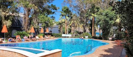 A swimming pool with lounge chairs and umbrellas, surrounded by palm trees and greenery.