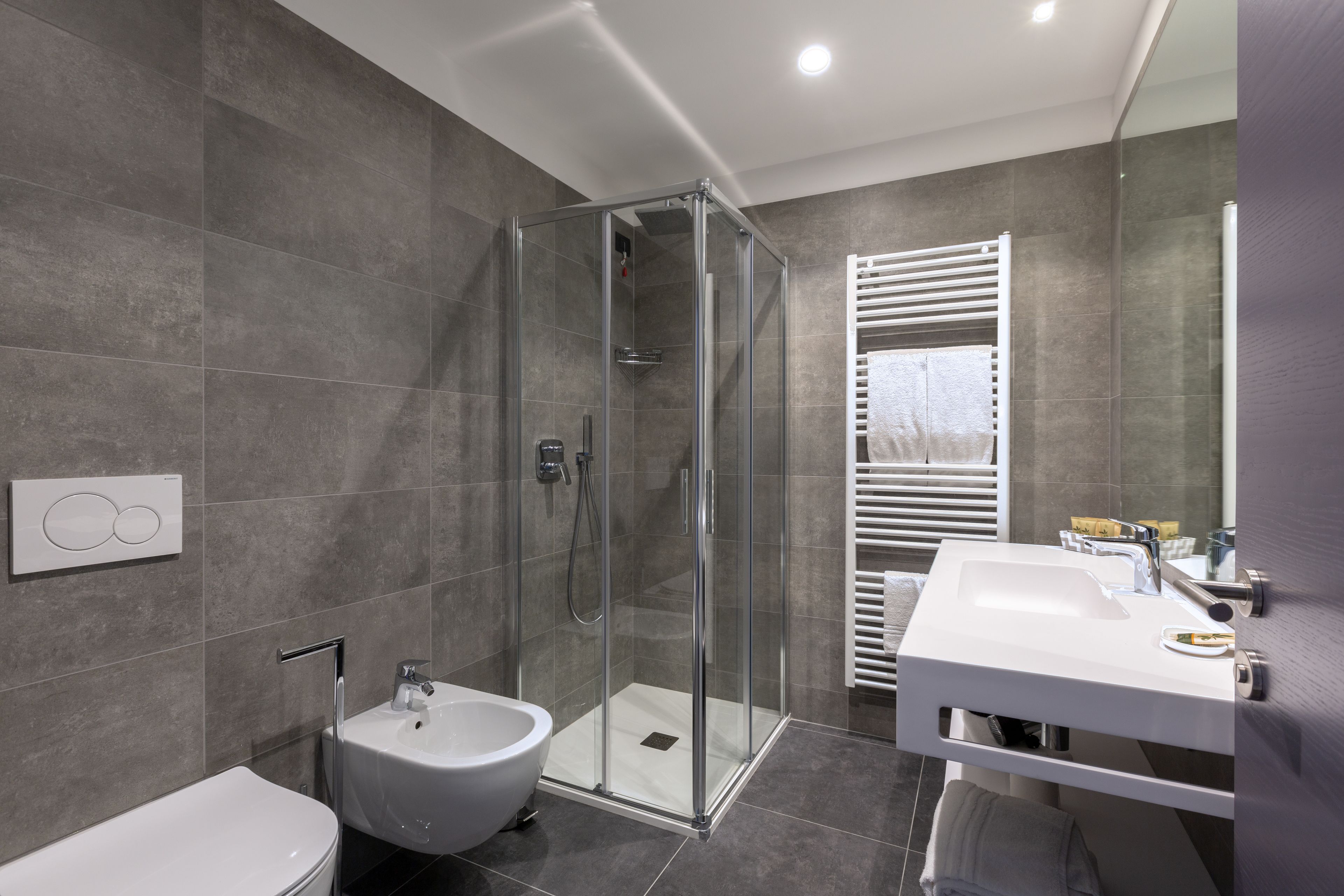 Un baño moderno con ducha de vidrio, lavamanos blanco y bidé.
