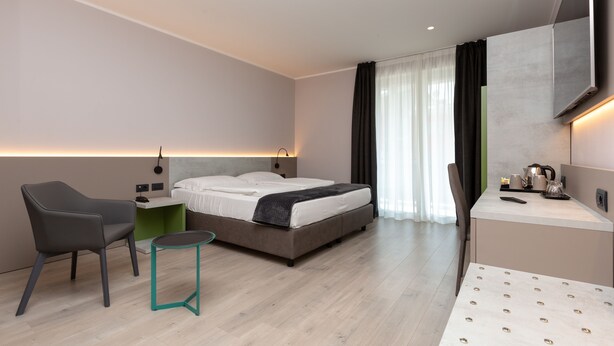 A modern hotel room with a bed, a desk, a chair, and a small table.