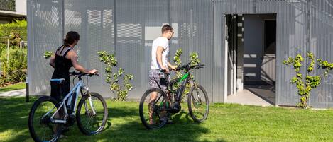 Dos bicicletas estacionadas en un área verde frente a un edificio moderno con fachada de malla.