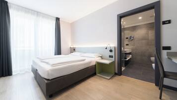 A modern hotel room with a large bed, bedside tables, a bathroom with a shower and toilet, and a view of the city.