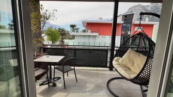 A balcony with a table and chairs, a hanging chair, and a view of buildings and mountains.