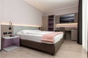Una habitación de hotel moderna con cama, mesita de noche, lámpara, televisión y estanterías empotradas.