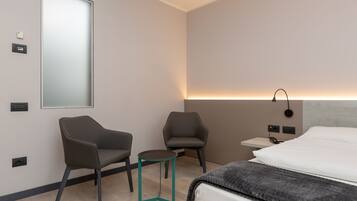 Ein modernes Hotelzimmer mit einem großen Bett, zwei Sesseln, einem kleinen Tisch und einem Nachttisch mit Lampe.