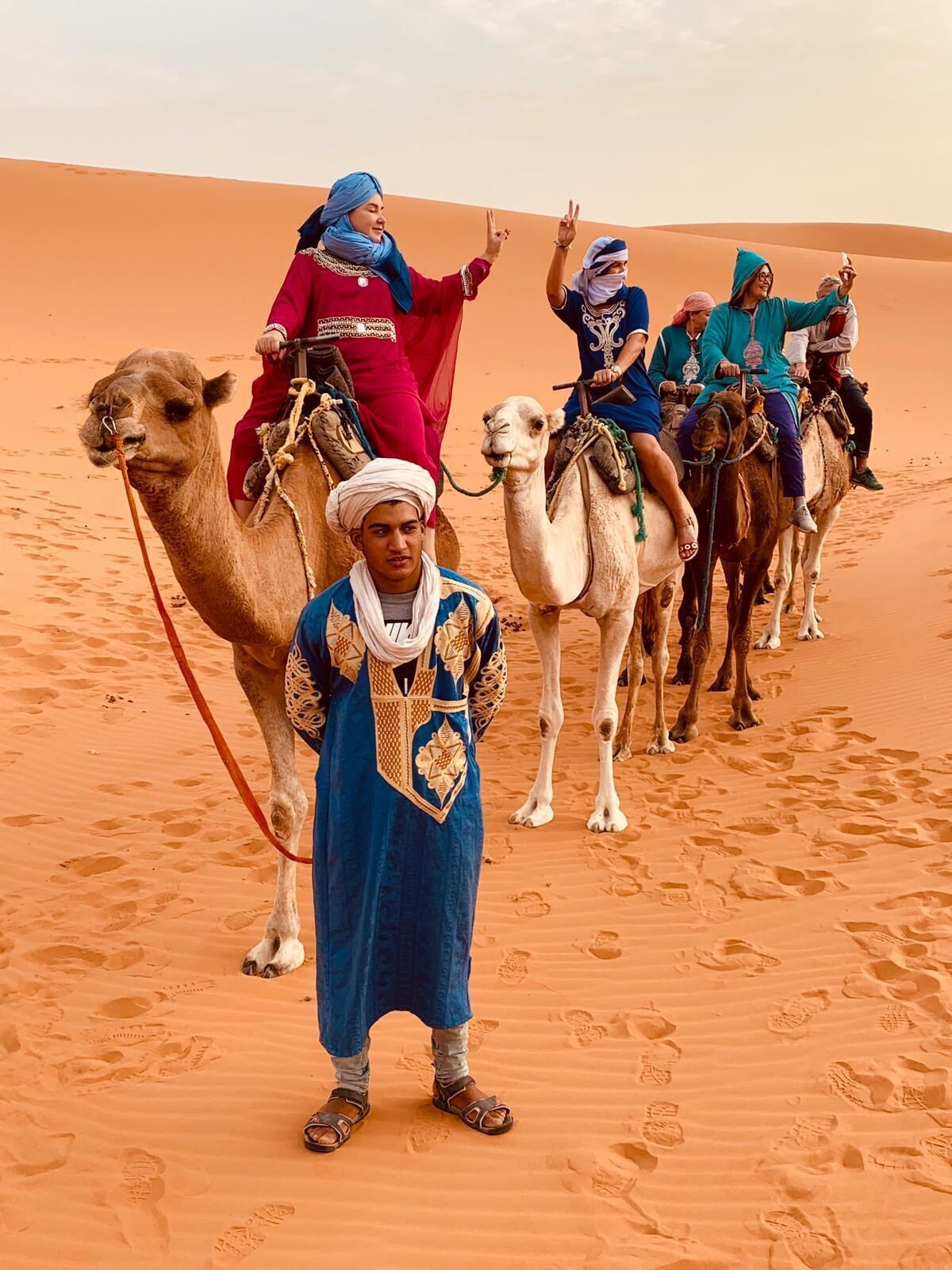 A group of people riding camels in a desert with sand dunes in the background.